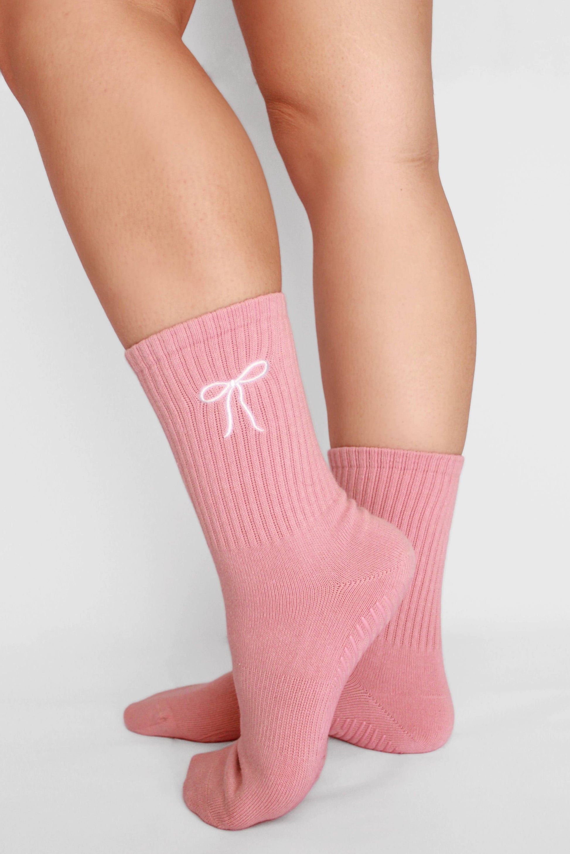 Pink socks with a white bow design worn by a person on a light gray background